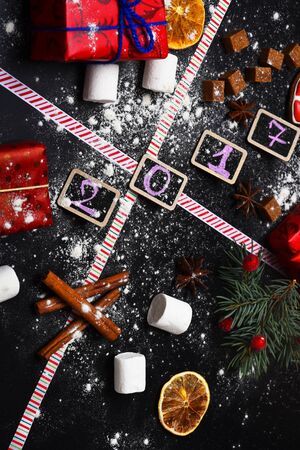 set of christmas or new year decoration with green fir tree with marshmallow, dry orange, anise, brown sugar and cinnamon with colorful presents or gifts on black backgroundの写真素材
