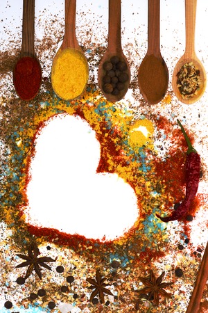 valentine set of ingredients for cooking spicy fragrant spices in spoons with allspice, coriander and pepper, laurel sheet, chili pepper, paprika in form of heart isolated on white, copy spaceの写真素材
