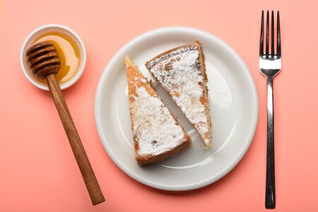 tasty slice of apple pies on white plate near silver fork, honey and stick on pink background, top...