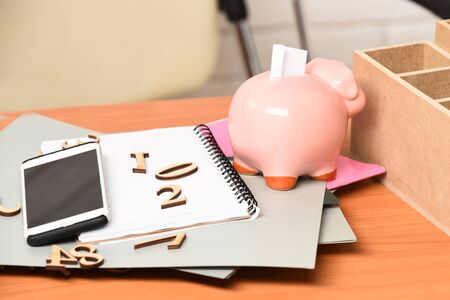 different papers with numbers, copybook, pink piggy pig bank and cell phone on brown wooden tableの写真素材