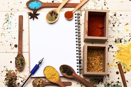 aromatic colorful spices in boxes and spoons with star anise cinnamon used in cuisine white copy book and pen on lactic vintage wooden background, copy spaceの写真素材