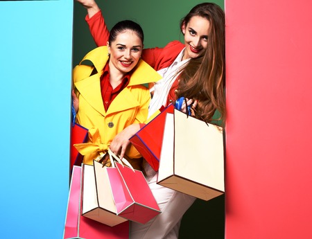 young sexy pretty funny women or model girls with long beautiful hair on happy face in colorful red and yellow coats with fashion makeup holding bags on green blue studio backgroundの写真素材