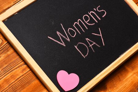 inscription Womens day painted by chalk with pink heart on black board on brown vintage wooden background, top viewの写真素材