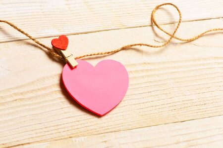 pink heart hanging with clothespin on clothesline on white vintage wooden backgroundの写真素材