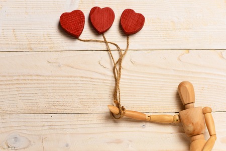 beautiful gestalta or poppet toy holding decorative valentine red hearts like balloons on white vintage wooden background, copy spaceの写真素材