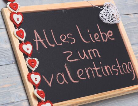 inscription "Alles liebe zum valentinstag" painted by pink chalk with valentine decoration on black board on blue vintage wooden backgroundの写真素材