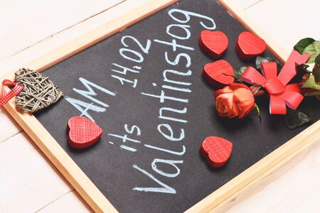 inscription in german painted by blue chalk with valentine beautiful orange roses with hearts on black board on white vintage wooden backgroundの写真素材