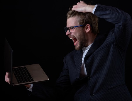 handsome bearded stylish angry business man in elegant black suit in glasses holding laptop in...