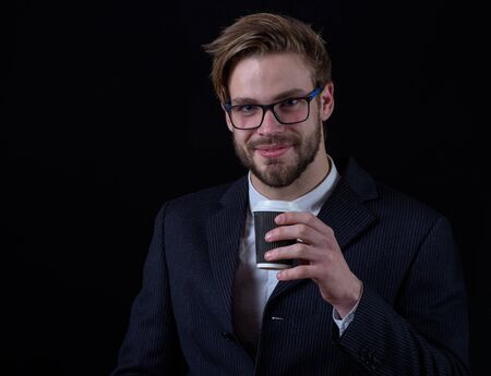 handsome bearded stylish smiling business man in elegant black suit in glasses holding cup of coffee in studio on black backgroundの写真素材