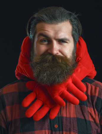 handsome bearded man or guy in checkered shirt with fashionable mustache and beard on confused face, with decorated hands of valentines red heart pillow on black backgroundの写真素材