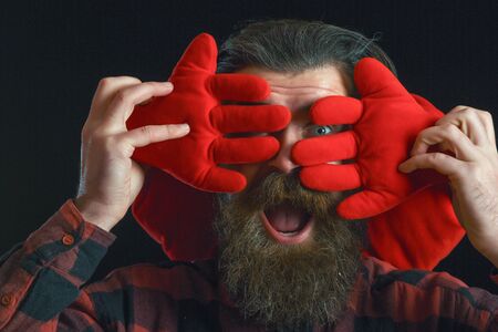 handsome bearded man or guy in checkered shirt with fashionable mustache and beard on happy face, with decorated hands of valentines red heart pillow on black backgroundの写真素材