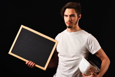 handsome bearded builder or foreman in white shirt on serious face holding board and helmet on black studio background, copy spaceの写真素材