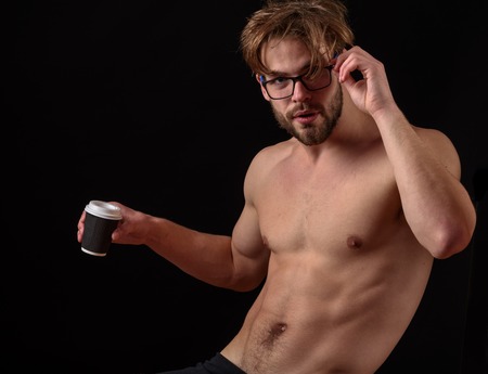 handsome bearded athletic macho man with stylish beard standing in glasses with muscle torso on athletic body holding hot coffee cup in studio on black backgroundの写真素材