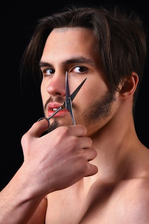 handsome bearded macho man portrait with stylish hair on serious face and naked chest holding scissors in studio on black backgroundの写真素材