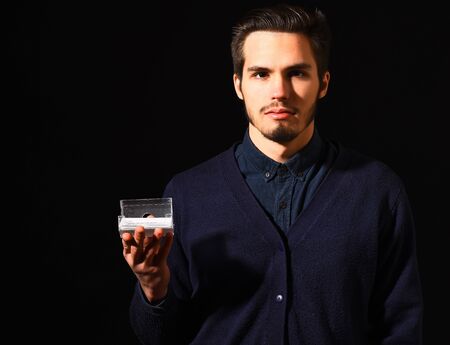 handsome bearded man in blue sweater with stylish hair on serious face holding box for visiting cards in black studio background, copy spaceの写真素材