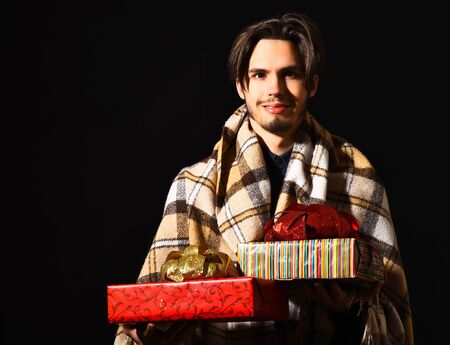 handsome bearded smiling man in checkered plaid holding colorful presents or gifts on black studio backgroundの写真素材