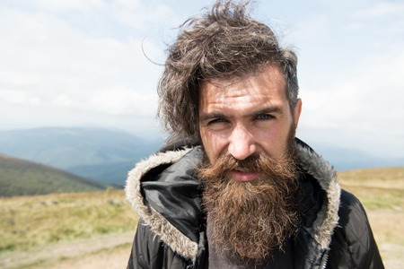 Handsome man hipster with beard and moustache portrait on mountain top against blue foggy cloudy skyの写真素材
