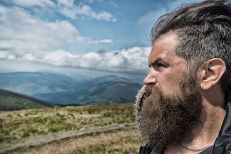 Handsome man hipster with beard and moustache portrait on mountain top against blue foggy cloudy skyの写真素材