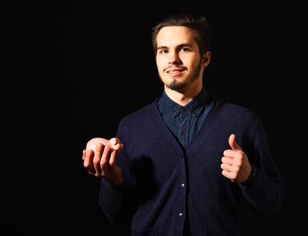 handsome bearded man in blue sweater with stylish hair on smiling face holding pink piggy bank in black studio backgroundの写真素材