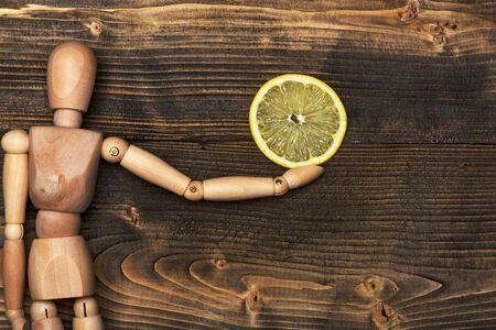 wooden puppet holding colorful fresh yellow lemon slice on brown vintage background, top viewの写真素材