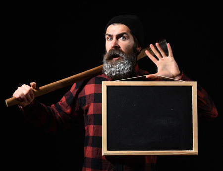 Surprised man or lumberjack, bearded hipster, with beard and moustache in red checkered shirt with axe and empty chalkboard or board isolated on black background, copy spaceの写真素材