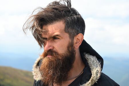 Handsome man hipster with beard and moustache portrait on mountain top against blue foggy cloudy skyの写真素材