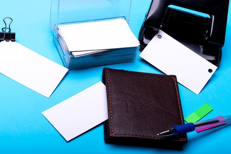 set of stationery for office: hole puncher, box with blanks, binder clip, wallet, pen, stickers on blue background, side viewの写真素材