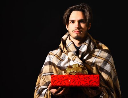 handsome bearded man in checkered plaid holding red present or gift on black studio backgroundの写真素材