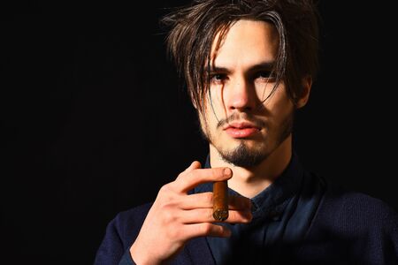 handsome bearded man portrait in blue shirt with stylish hair on serious face holding cigar in black studio background, copy spaceの写真素材