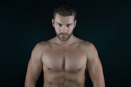 handsome unshaven macho man or sexy muscular guy with athlete body and torso, has beard on serious face on black backgroundの写真素材