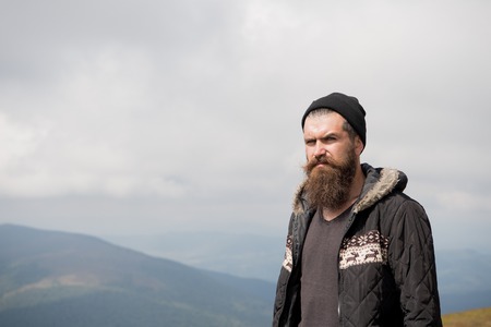 Handsome man hipster or guy with beard and moustache on serious face in hat and jacket sunny outdoor...