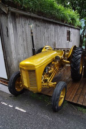 Norway - January 25, 2010: old yellow farm tractor stands near wooden barn with grassy roof outdoors on summer dayのeditorial素材