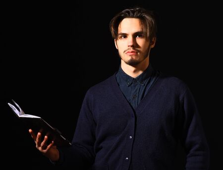 handsome bearded man in blue sweater with stylish hair on serious face holding notebook in black studio background, copy spaceの写真素材