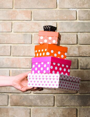 colorful polka dot box of spotted paper in female hand as holiday present or gift on brick wall...