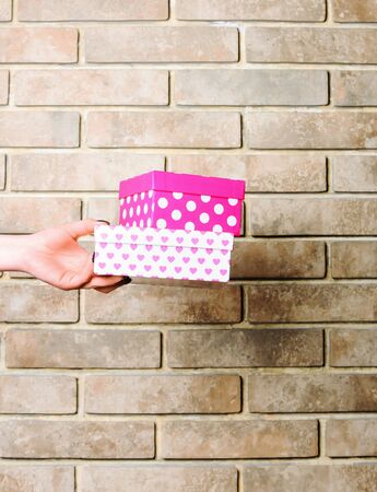 colorful polka dot box of spotted paper in female hand as holiday present or gift on brick wall...