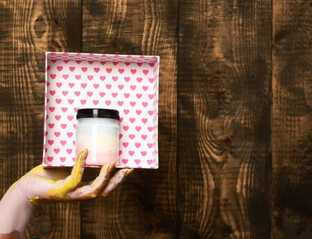 female hand smeared in golden paint or glister holding handmade pink polka dots valentine box with...