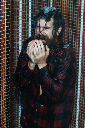 Energized handsome man, bearded hipster with beard and moustache in red checkered shirt pours ice...