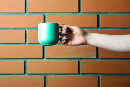 blue color tea or coffee cup or ceramic mug for drink as morning refreshment in female hand on textured brown brick wall background, copy spaceの写真素材