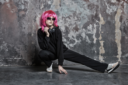 young pretty woman or sexy girl with hair wig pink color in glasses and music headset, wears black cloth on grey wall background, copy spaceの写真素材