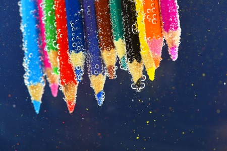 colored pencils in sparkling water on dark blue background with colorful bokeh, side viewの写真素材