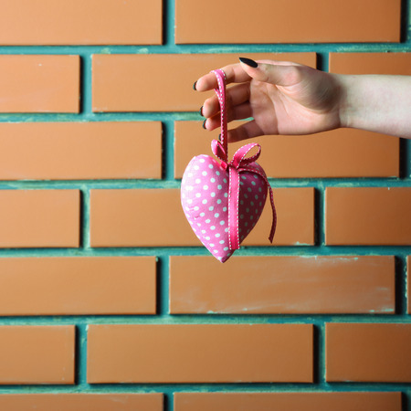 pink color handmade heart or valentines day holiday decoration in female hand as present or gift on brick wall background, copy spaceの写真素材