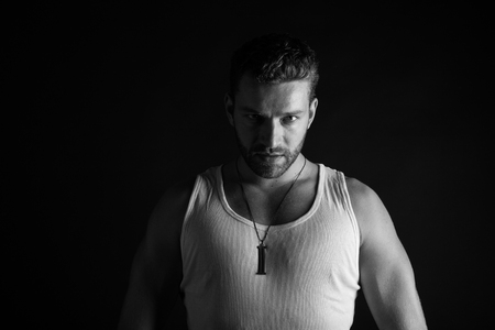 young handsome bearded man sexy macho with muscular hands and beard on serious face in white vest posing in studio on black background, black and whiteの写真素材
