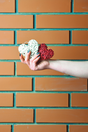 red and white color handmade straw heart or valentines day holiday decoration in female hand as present or gift on brick wall background, copy spaceの写真素材