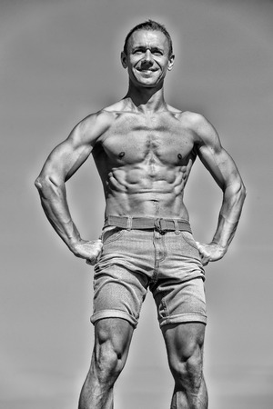 handsome man with sexy muscular body in shorts training sport, has smiling happy face, posing outdoor sunny summer on sky background, black and whiteの写真素材