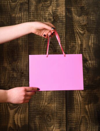 pink color paper shopping bag or package in female hands as holiday present or gift on wooden background, copy spaceの写真素材