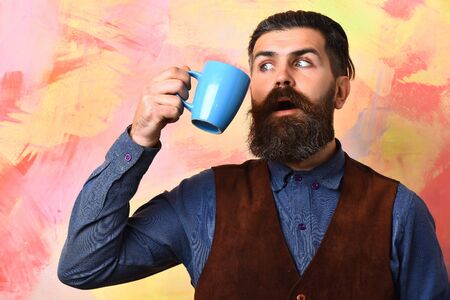 Bearded man, long beard. Brutal caucasian surprised hipster with moustache holding blue coffee cup...