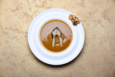 cream soup or puree brown color with fish and fried onion rings on white plate on beige background