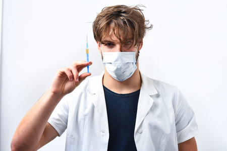 Brutal caucasian serious doctor or unshaven hipster, postgraduate student holding syringe in mask and medical gown isolated on white background.の写真素材