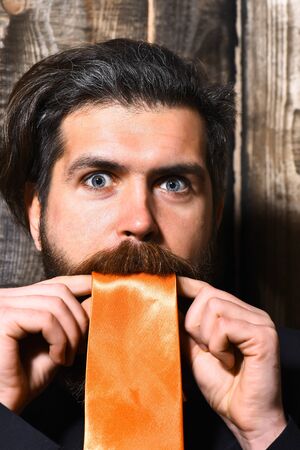 caucasian shouting hipster with moustache in suit holding acid orange tie on brown vintage wooden studio backgroundの写真素材