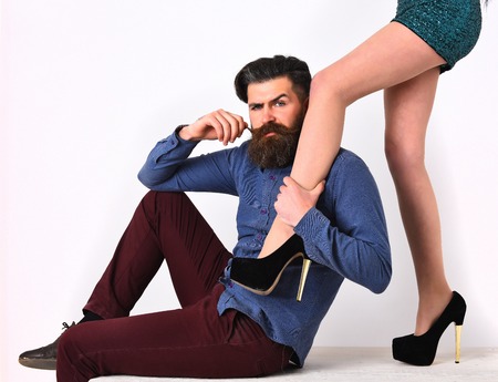 caucasian hipster with moustache on serious face with female sexy legs in fashionable shoes and green sequins skirt isolated on white background getting haircutの写真素材